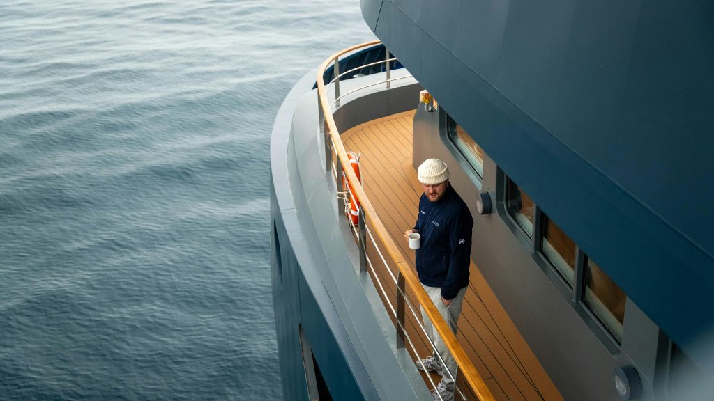 Man enjoys coffee on yacht deck overlooking the serene sea, providing a sense of adventure and relaxation.