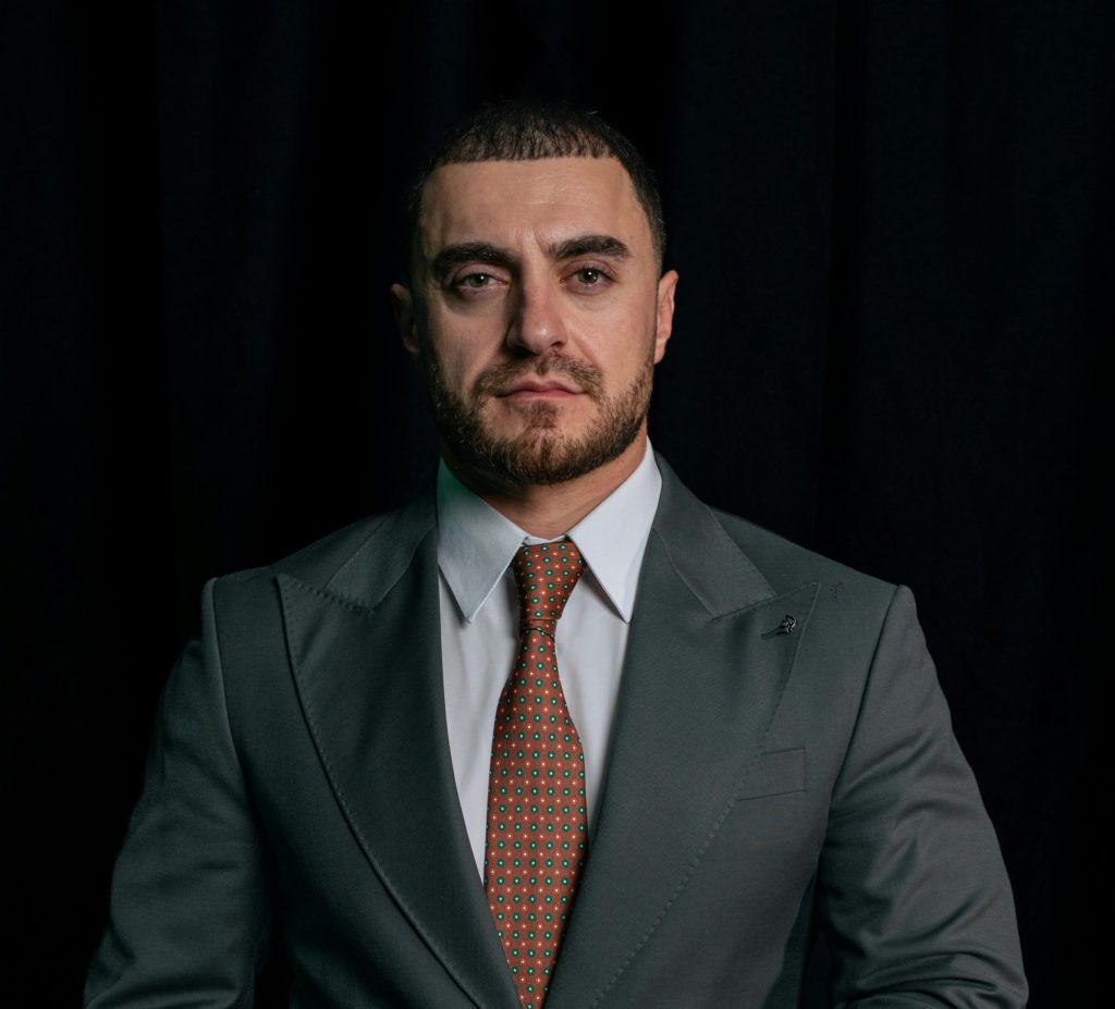 Portrait of a confident businessman in a formal suit against a dark backdrop.